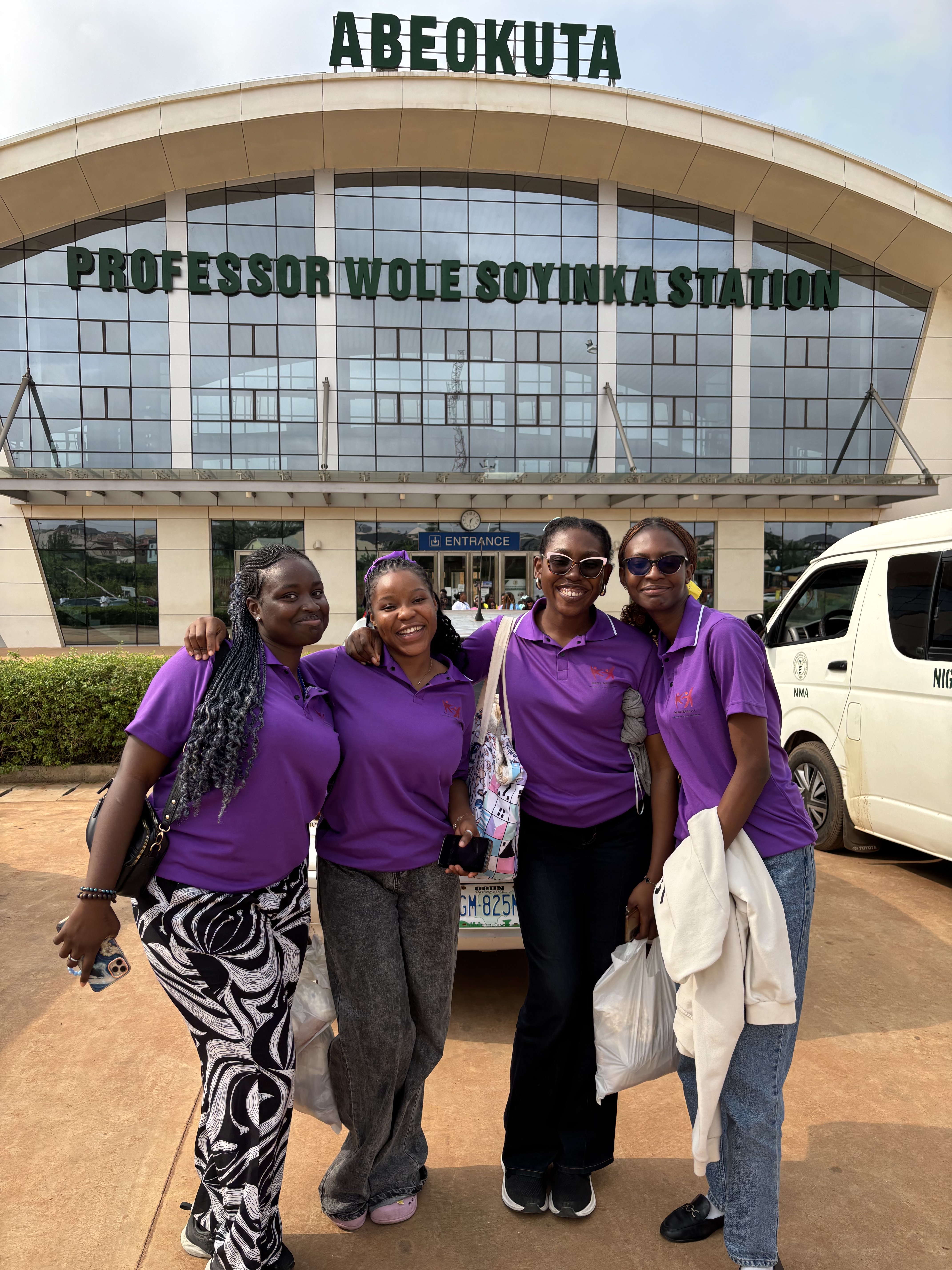 Four volunteers in purple shirts posing together at Abeokuta Professor Wole Soyinka Station during a cultural excursion